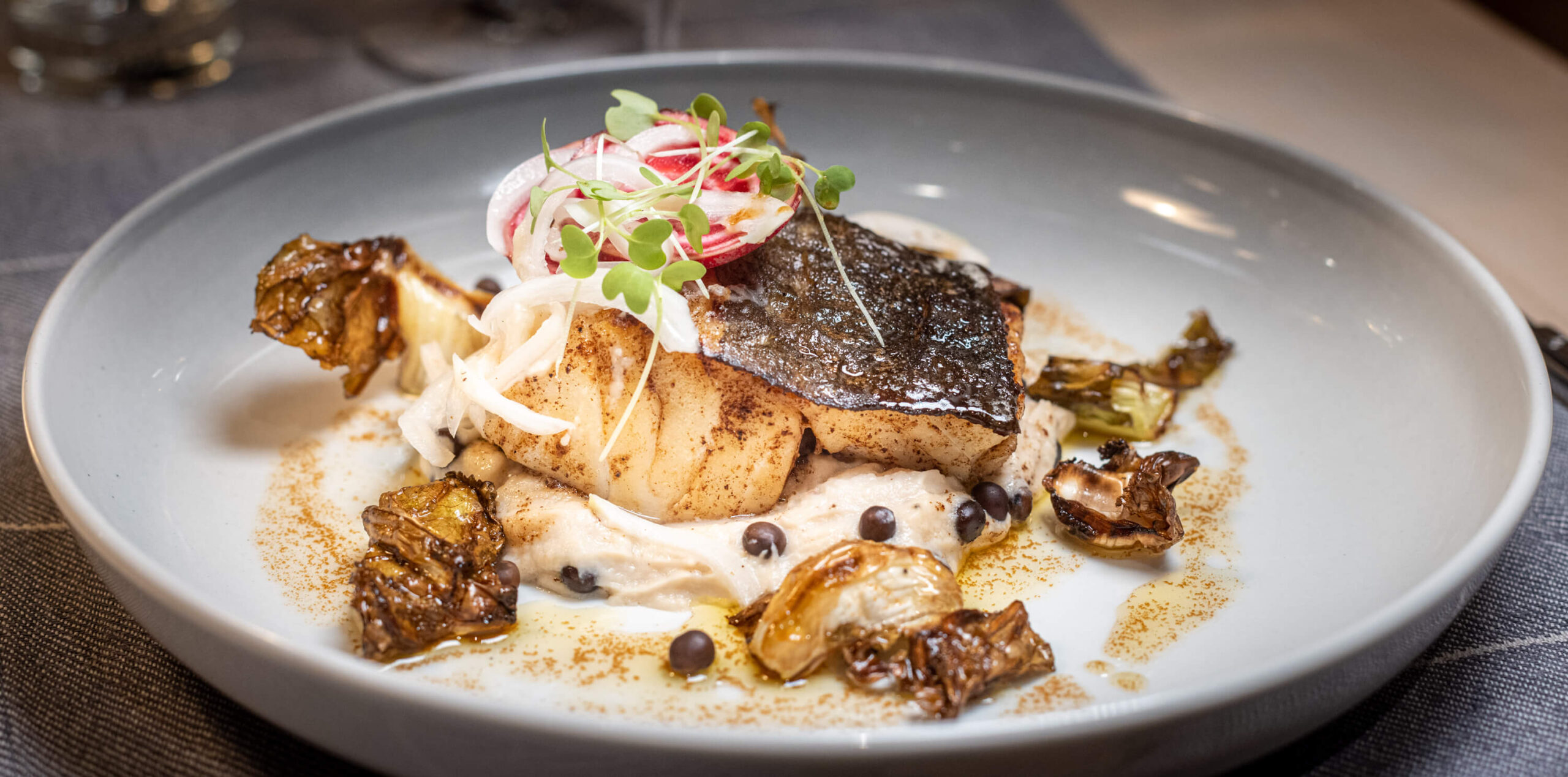 Plated meat dish with creamy sauce, sliced potatoes, and pickled salad garnish on a restaurant table