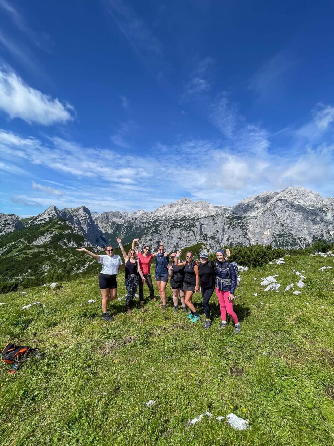 Women hiking together on a grassy trail with alpine mountains and peaks under a blue sky in Europe