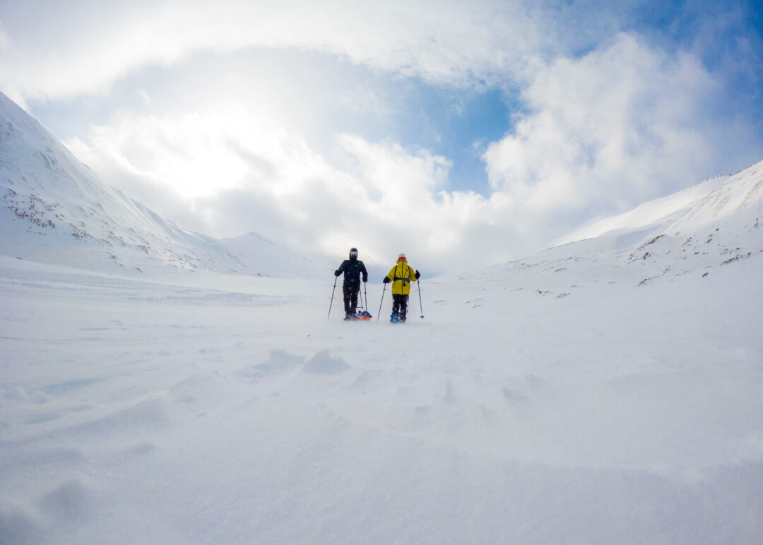 Women snowshoeing across snowy Arctic mountains in a wide valley