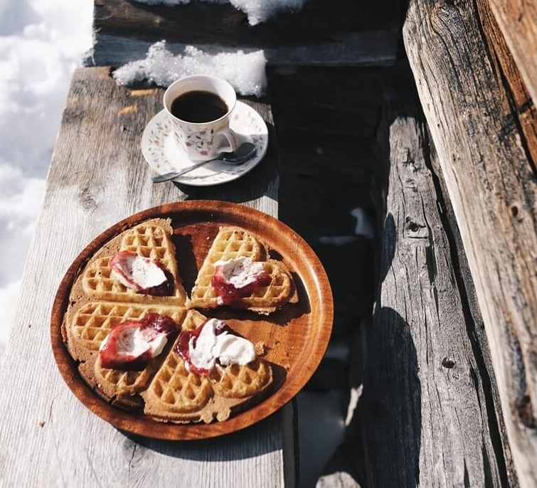 Waffles and coffee on a wooden table in a snowy outdoor setting
