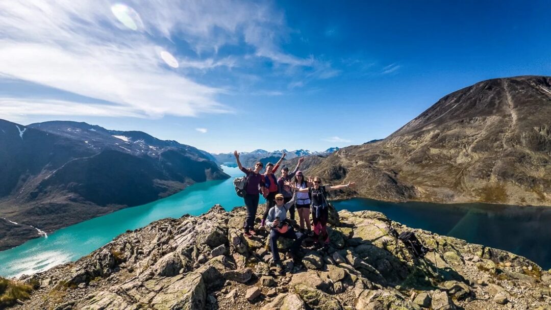 Women hikers pose on a rocky summit overlooking a turquoise fjord in Norway