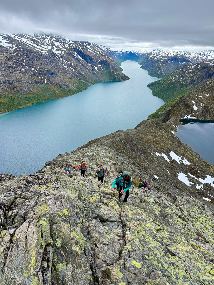 Hikers on a rocky ridge overlooking a Norwegian fjord valley and glacier in the distance