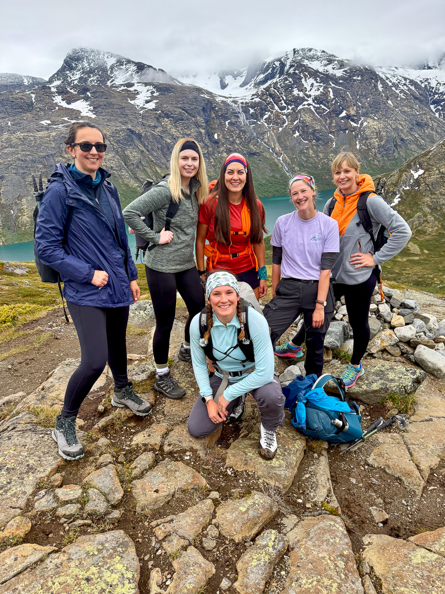 Women hikers posing on a rocky mountain trail with snowy peaks in Norway during a hiking adventure