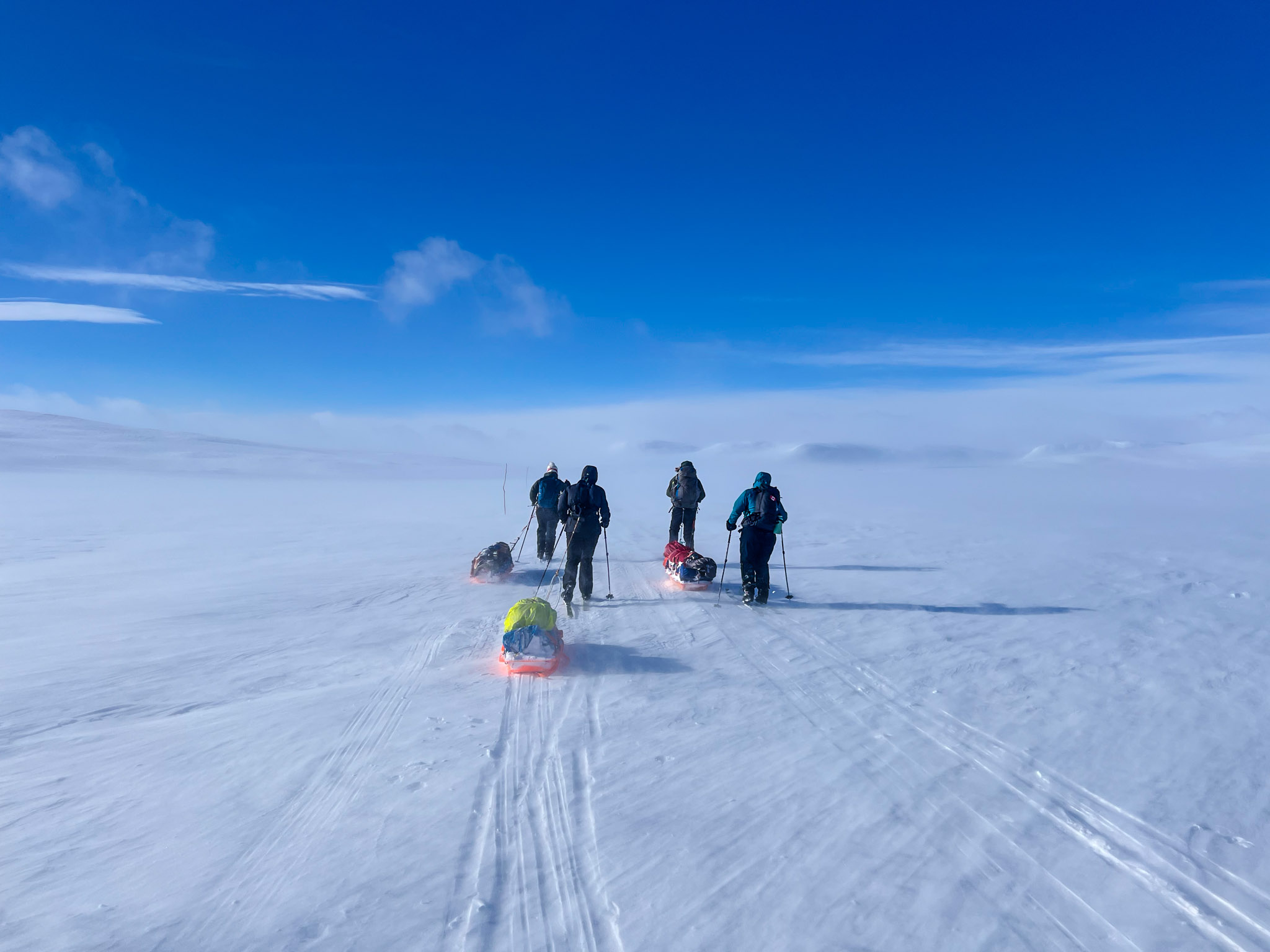 Women ski-hiking with sleds across snow-covered Arctic tundra under a clear blue sky