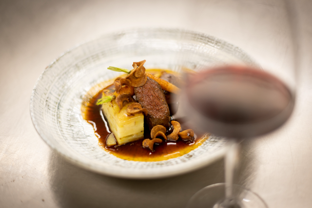 Hand pouring sauce over a mushroom and pork dish in a bowl