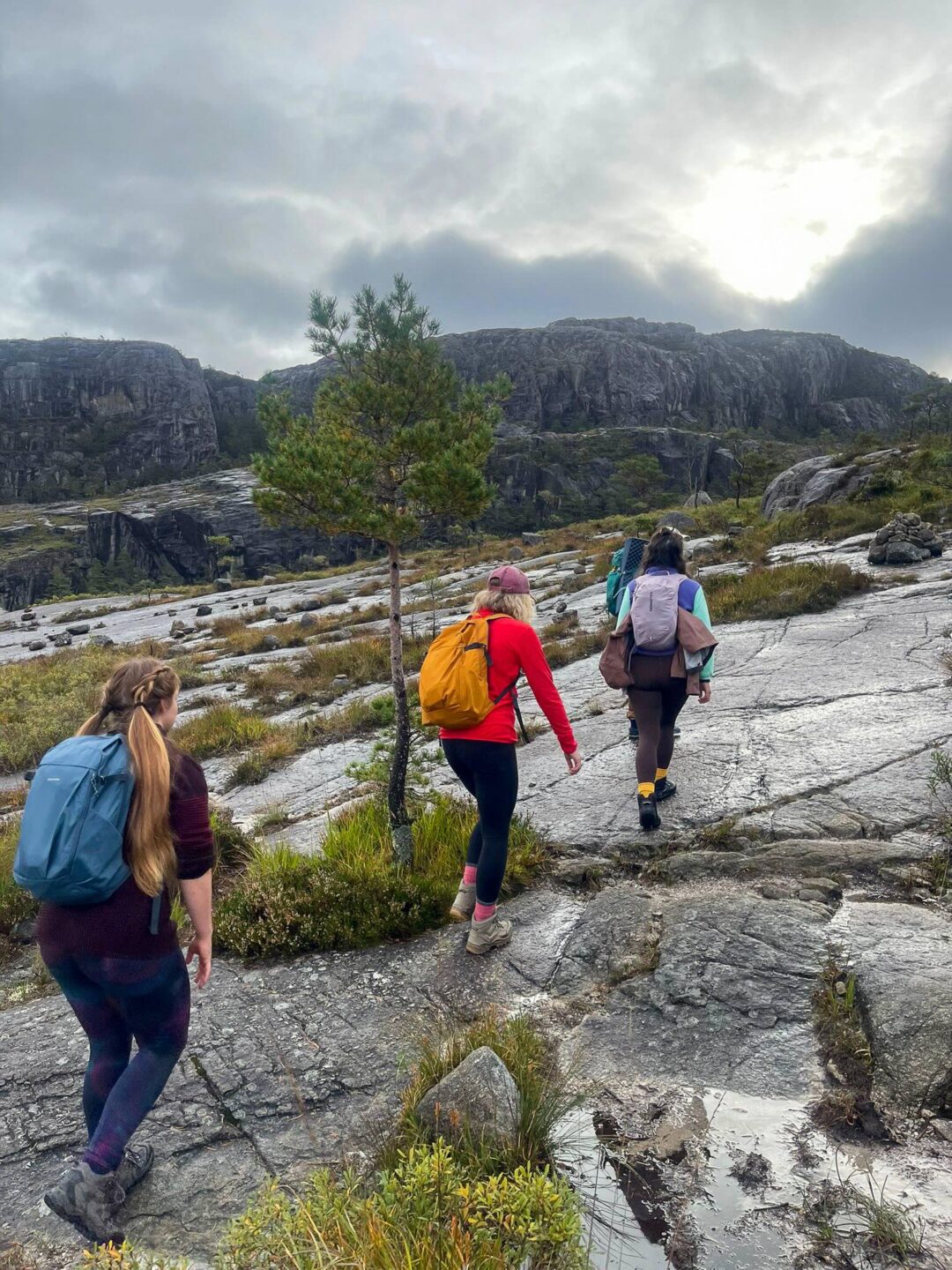 Women hiking on rocky trail with fjord cliffs in Norway under cloudy skies