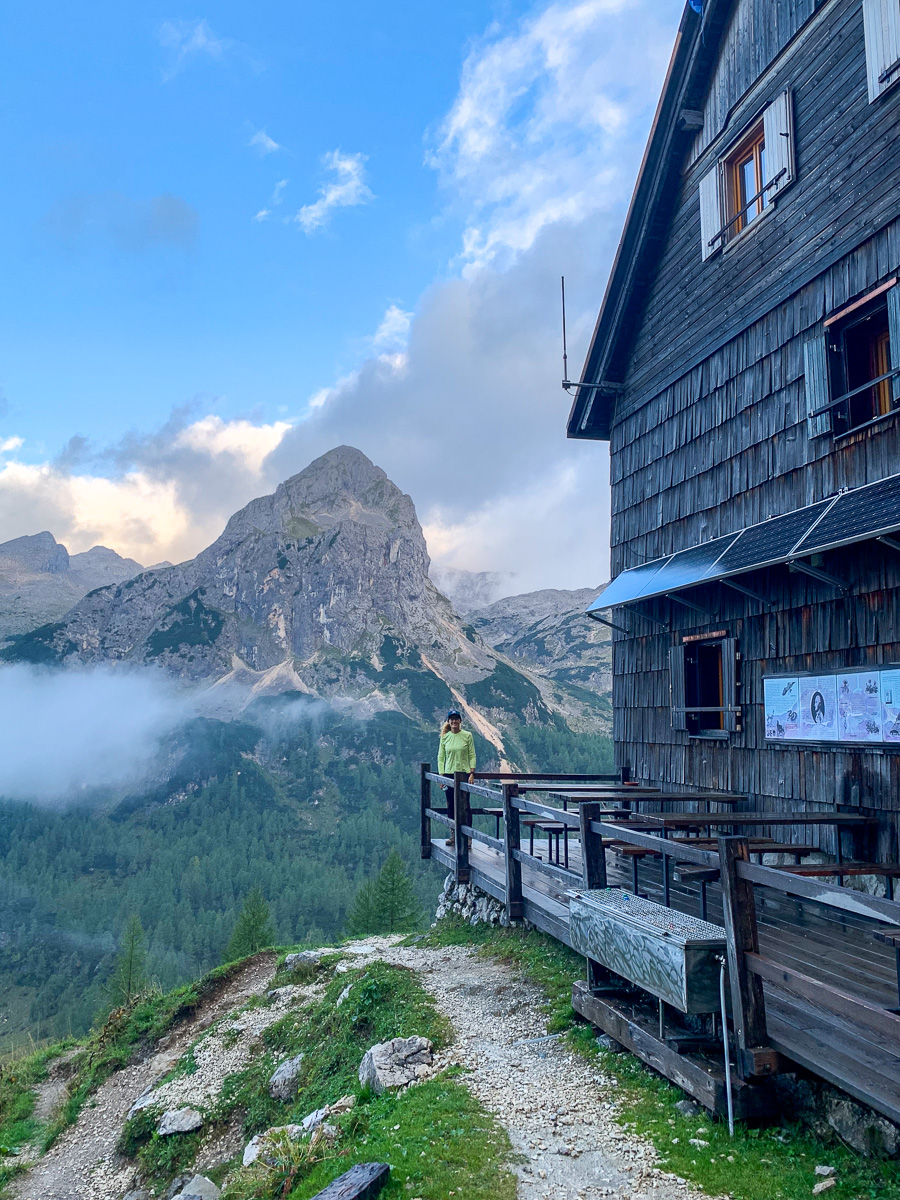 Woman on a hiking trail beside a wooden mountain hut with Alpine peaks in Slovenia