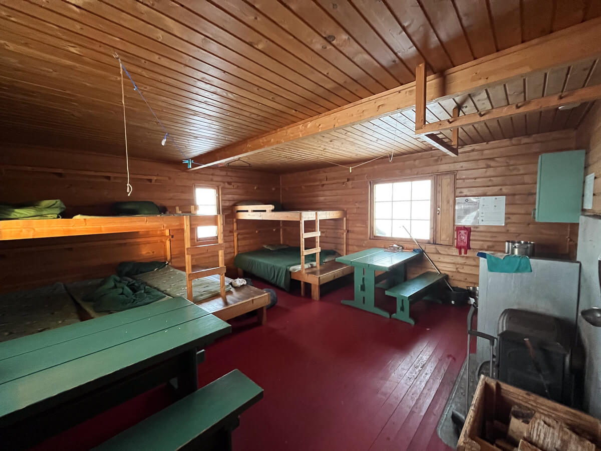 Wooden ski hut interior with bunk beds, seating and a table.