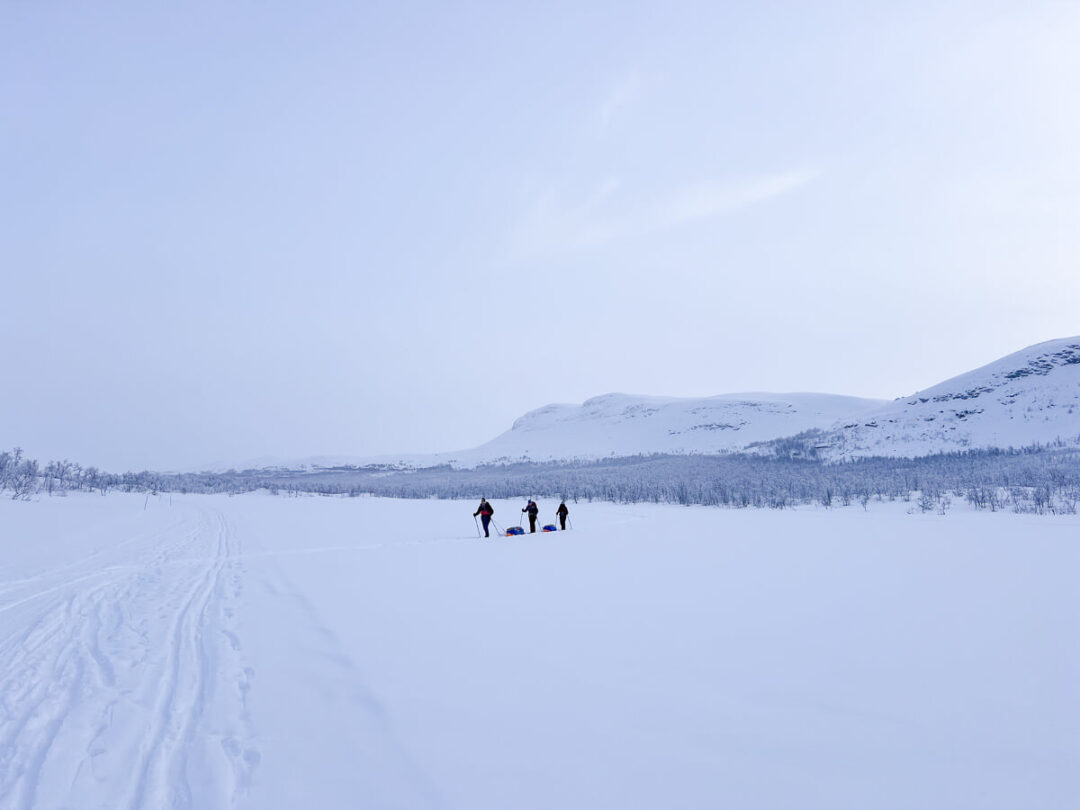Skiers on a snowy trail across an Arctic landscape during a hut-to-hut ski expedition