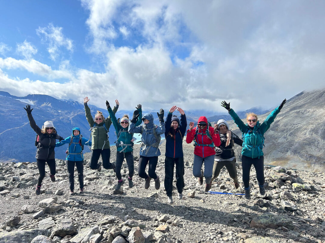 Women hiking on a rocky mountain trail in Norway, group at the summit with arms raised