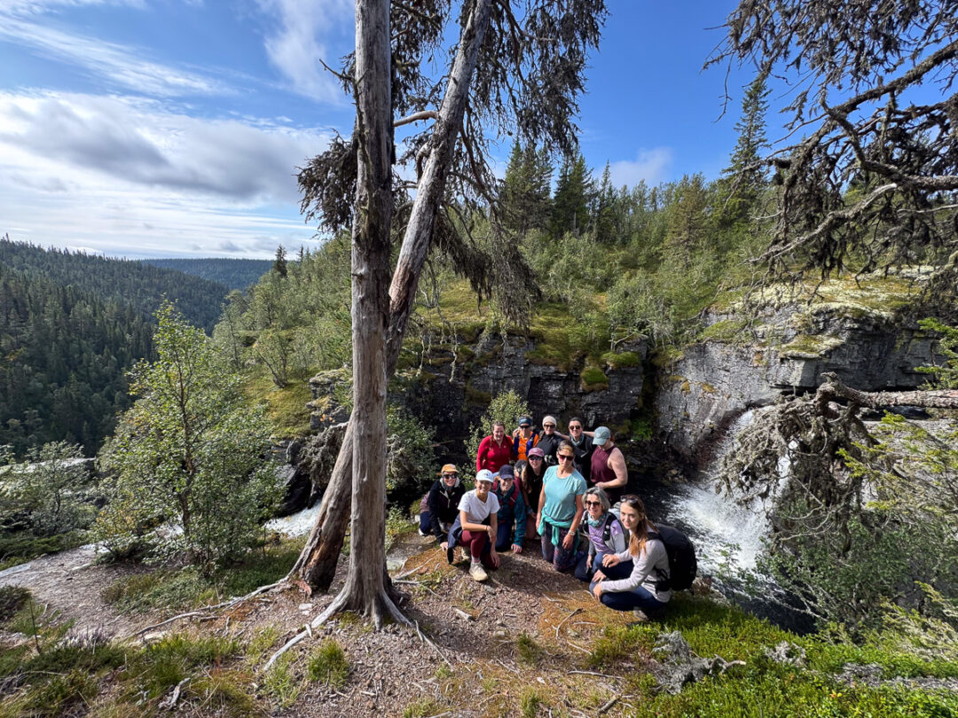 Women hiking group posing by a waterfall in a Norwegian forest landscape outdoors