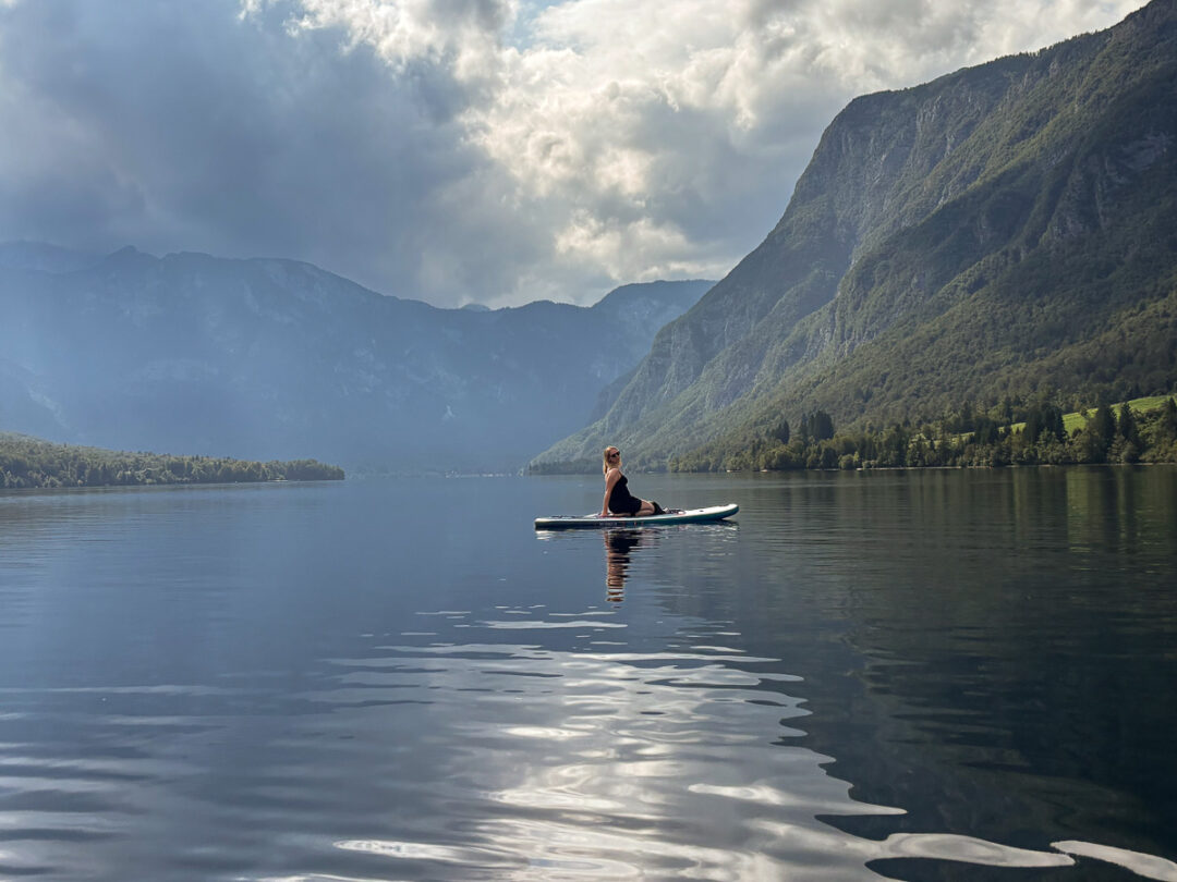 Woman kayaking on a calm mountain lake in Slovenia, surrounded by forested peaks and misty hills