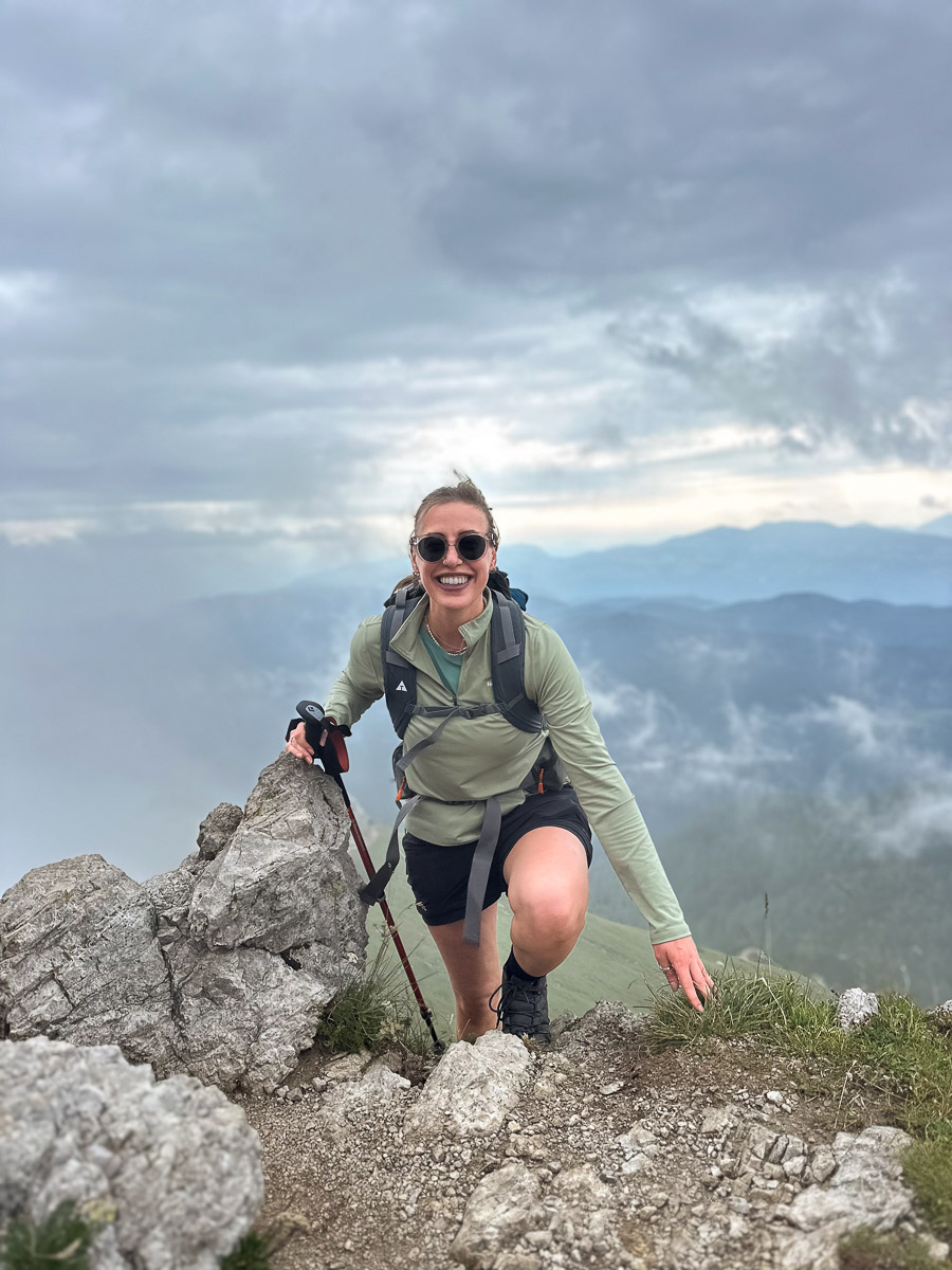 Women’s hiking trek on a rocky mountain summit, with cloudy valley views and distant peaks.