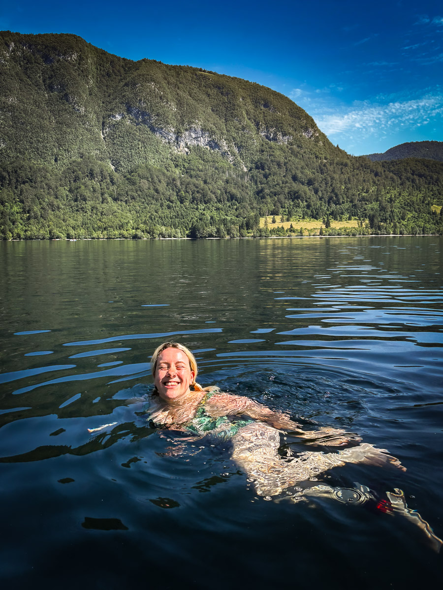 Woman swimming in a mountain lake with forested hills and cliffs in Slovenia