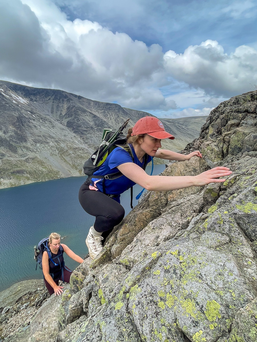 Women hikers with backpacks on a rocky ridge overlooking a mountain lake and clouds