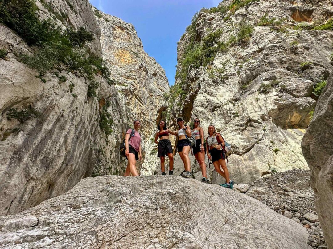 Women hiking through a narrow rocky canyon trail in East Sardinia