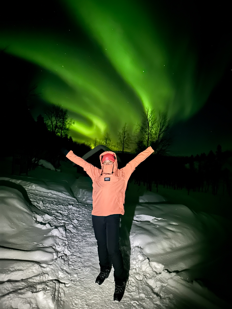 Women’s ski trip: woman in snowscape with Northern Lights overhead in the Arctic region