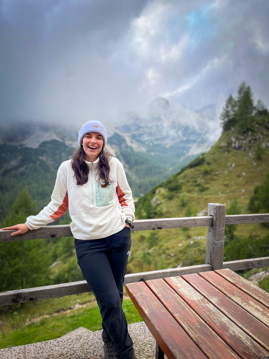 Woman hiking on a wooden lookout above alpine valleys, Slovenia, with misty mountains in the background.
