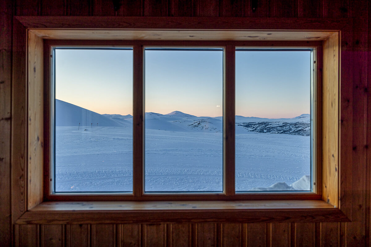 Snowy mountain landscape seen through a wooden cabin window at sunrise