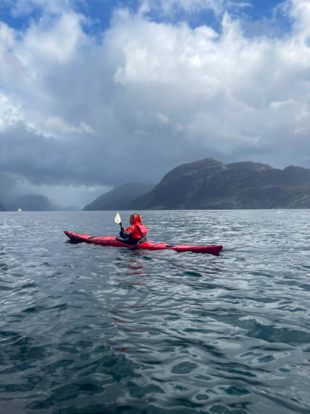 Woman kayaking on calm fjord water with mountains and cloudy sky in the background
