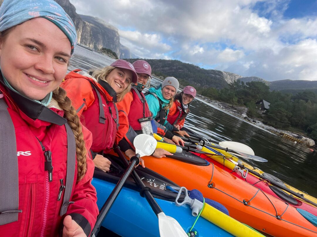 Women kayaking on an orange kayak in Norway, smiling in a group with lifejackets and paddles