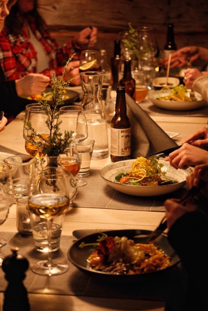 Women dining together at a candlelit table with plates of food and wine bottles indoors