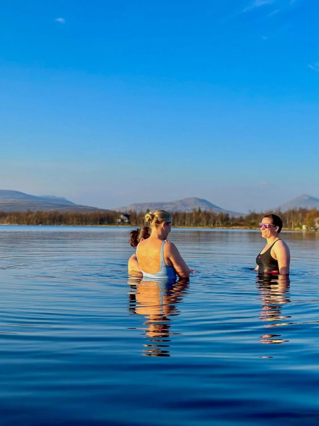 Women wading in a calm lake with mountain views in the background during an outdoor adventure hike trip