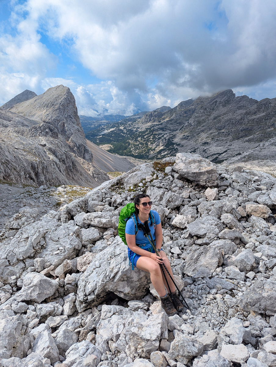 Woman hiking on a rocky mountain trail in the Slovenian Alps, with a valley view under cloudy skies