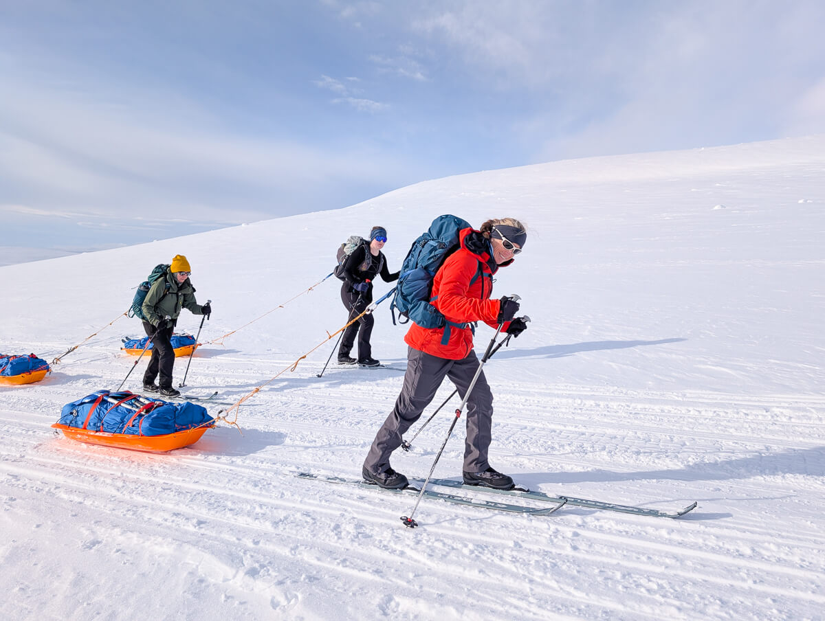 Women ski touring across snowy Arctic landscape, pulling sleds on a hut-to-hut route