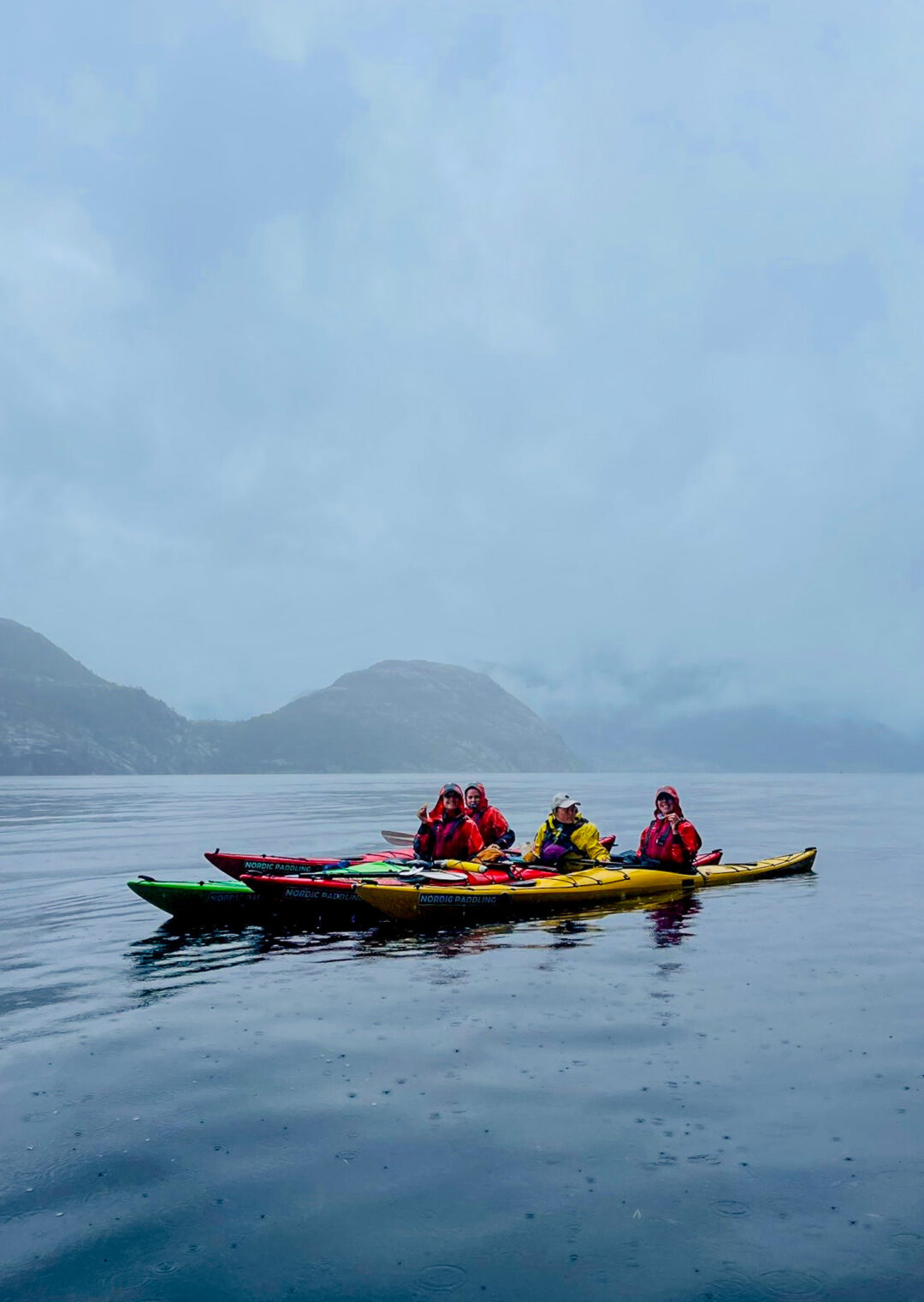 Women kayaking in a Norwegian fjord, group paddling on calm water in bright kayaks
