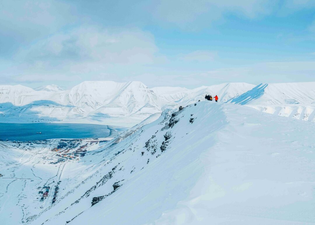 Women snowshoeing across snowy ridge in Svalbard with Arctic mountains and sea in the distance