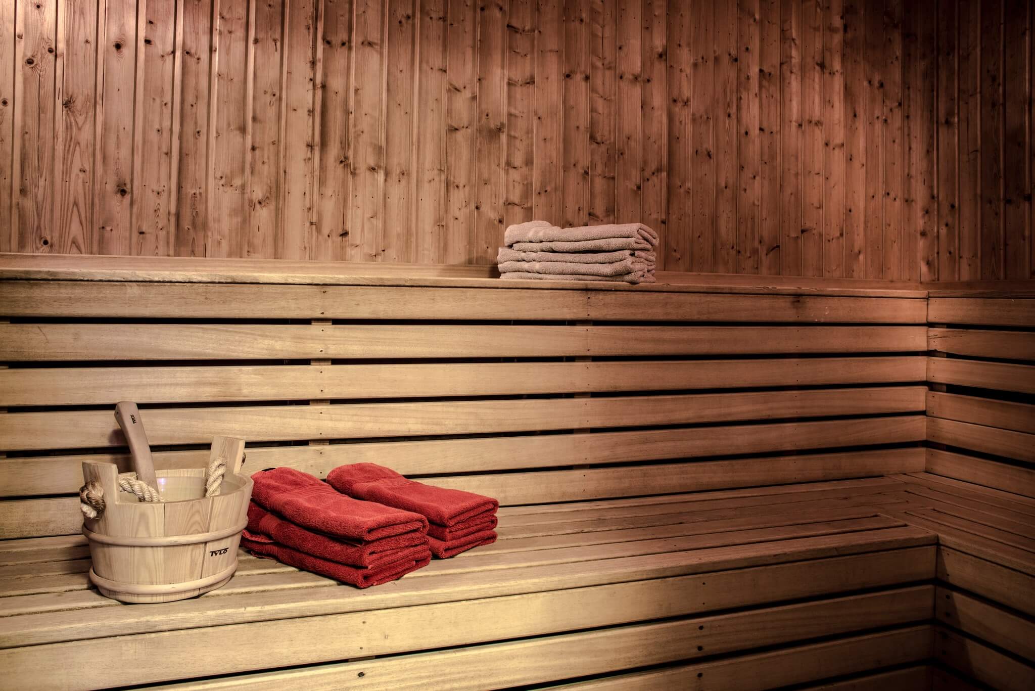 Sauna room with wooden benches, folded red towels and a water bucket