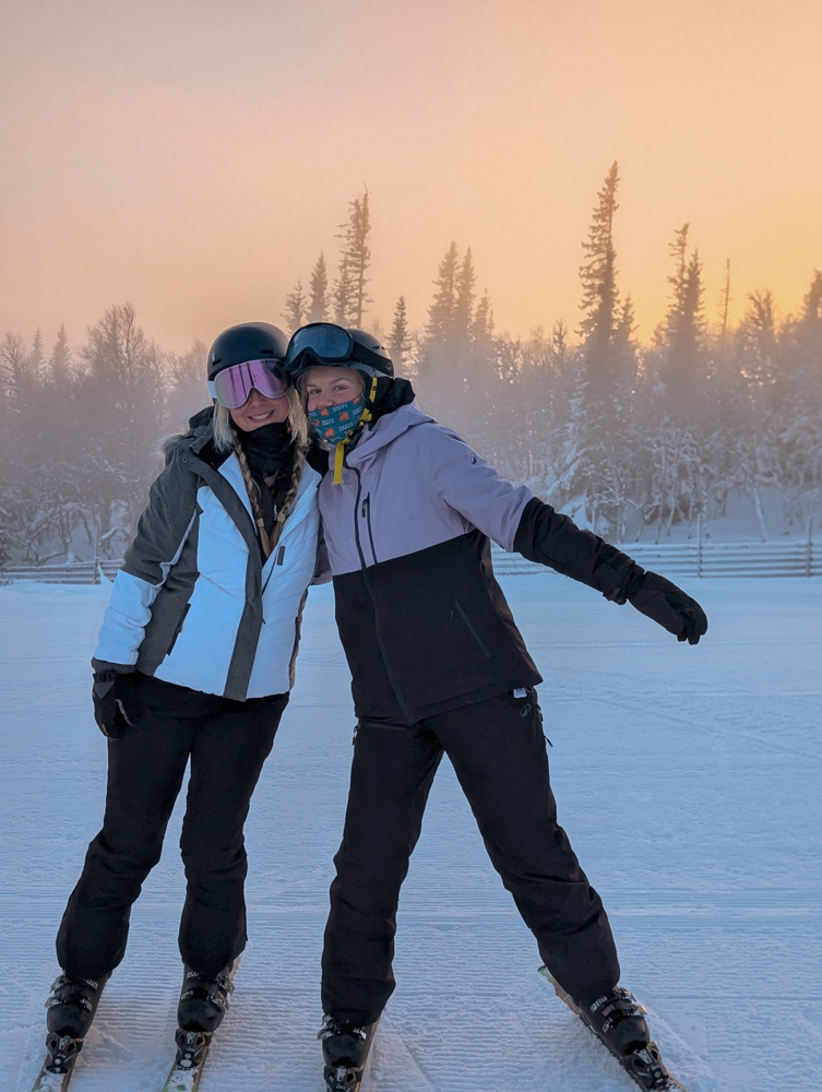 Two women downhill skiing on a snowy slope in a winter forest landscape