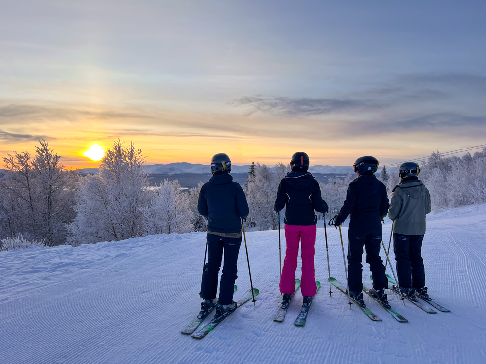 Women downhill skiing on a snowy slope at sunset, standing with skis and poles in winter scenery