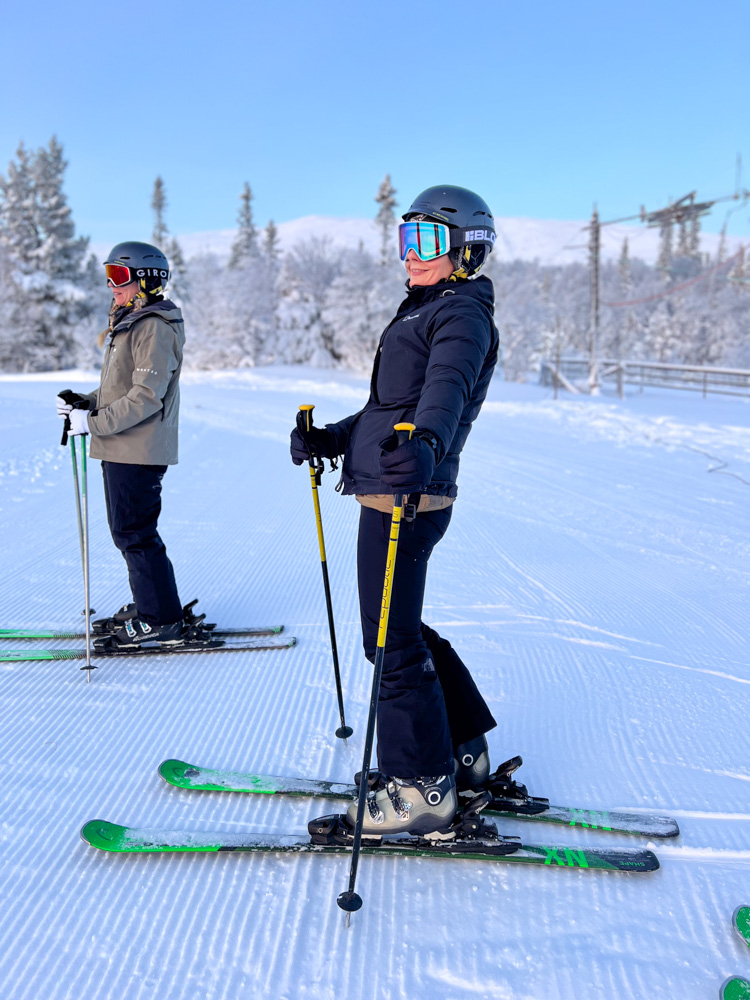 Women skiing downhill on a snowy slope, wearing helmets, goggles and skis.