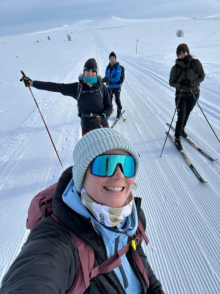 Women on cross-country skis on a snow trail in Sweden, taking a group holiday photo on ski tracks.