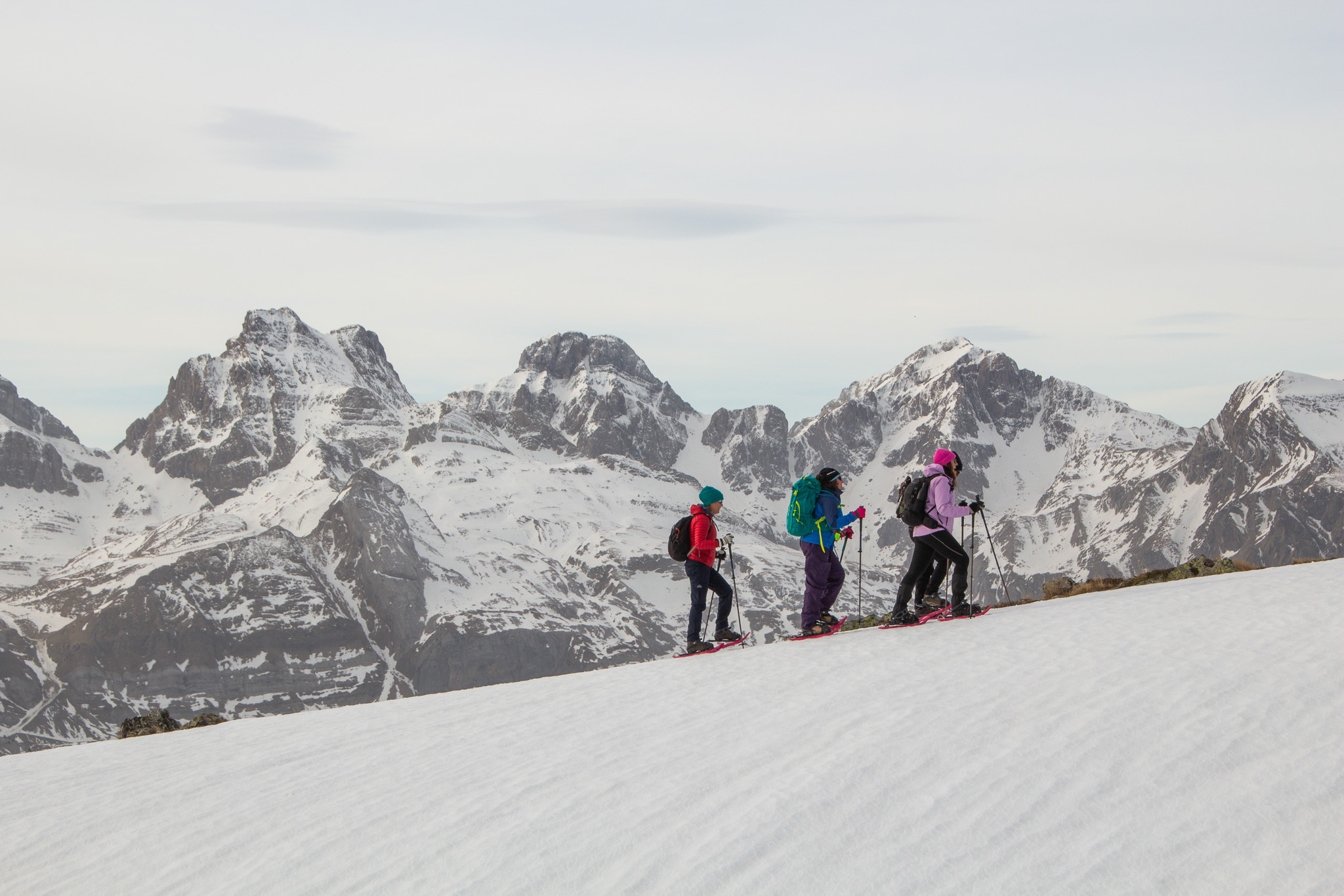 Women snow trekking on a snowy mountain slope, with a snowy mountain range in the background