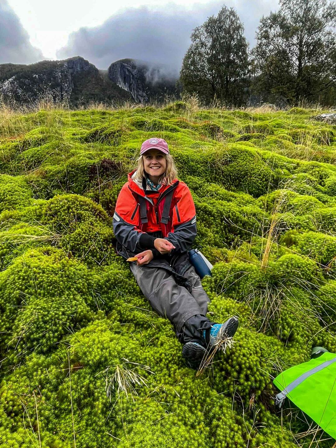 Woman sitting in lush mossy terrain with a tent and mountains in the background, outdoors in Norway