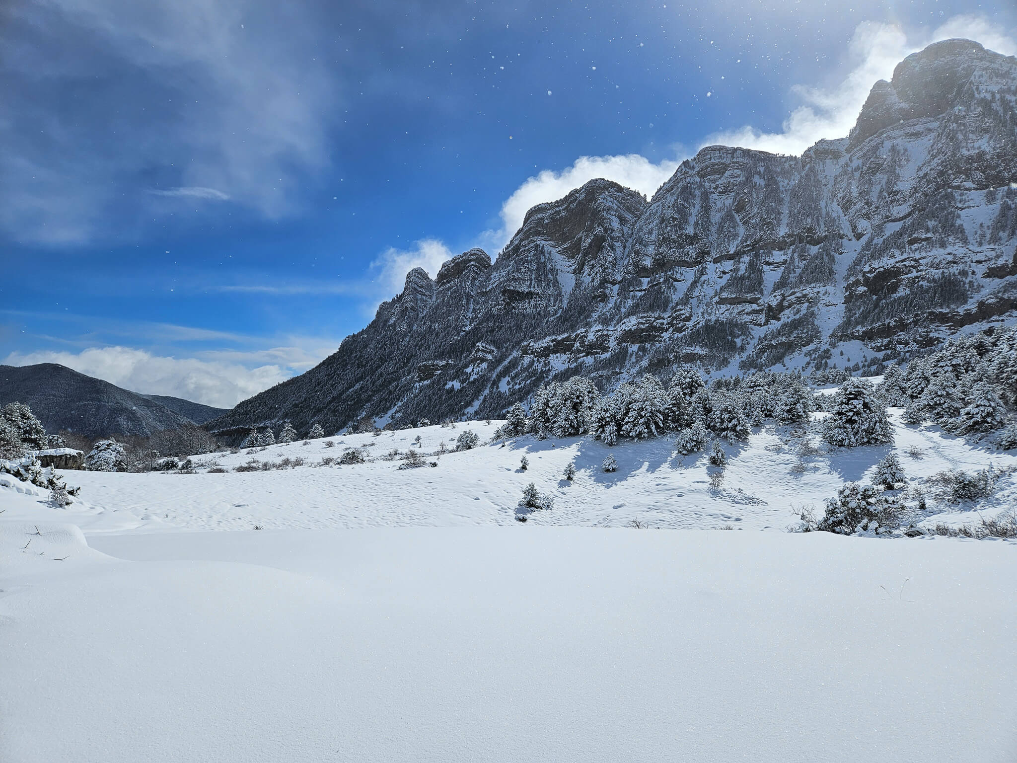 Snow-covered Alpine mountain valley with steep peaks and frosted trees under a blue sky