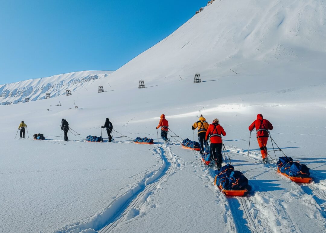 Women snowshoeing with guides and sleds on Arctic route in snowy Svalbard mountains