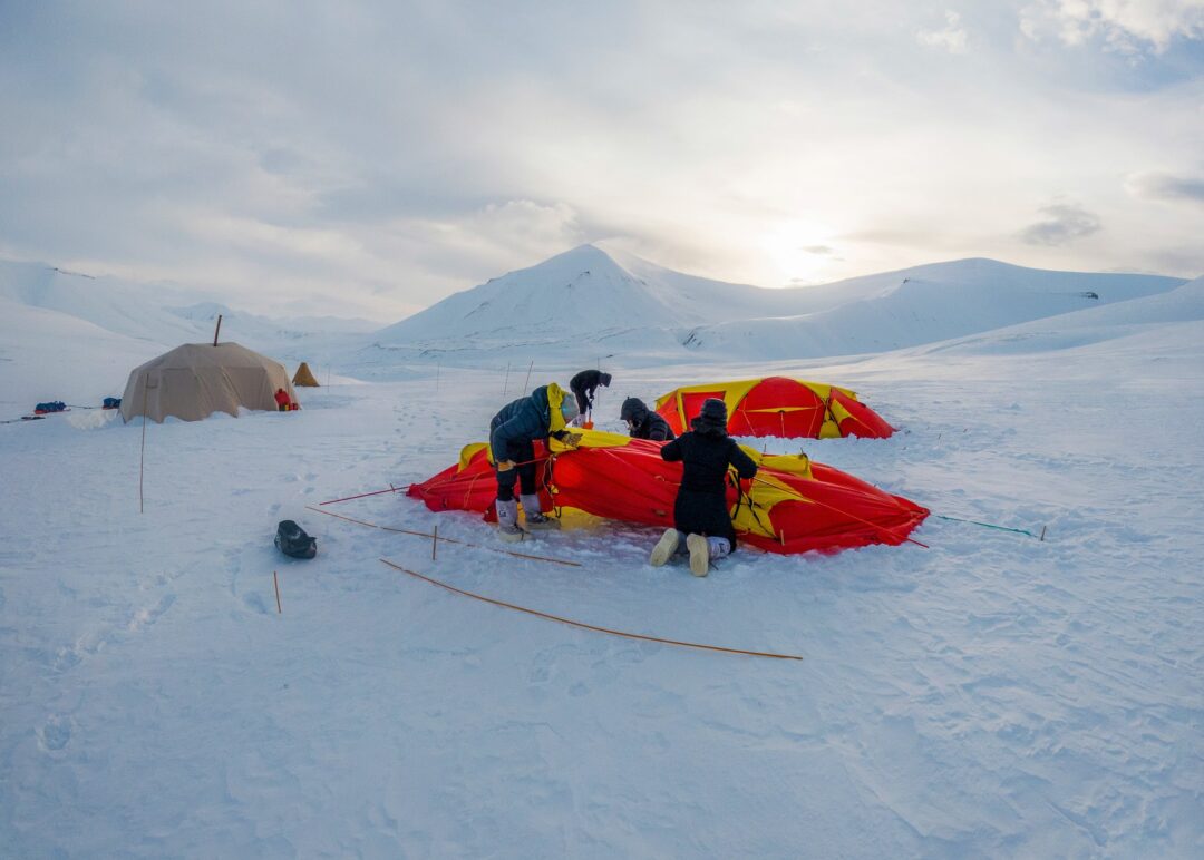 Women’s wild camping in snowy Arctic mountains with tents and winter expedition gear