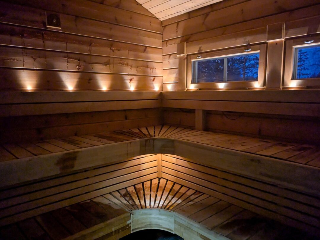 Wooden sauna interior with warm lighting and a tiled hot tub beneath the benches