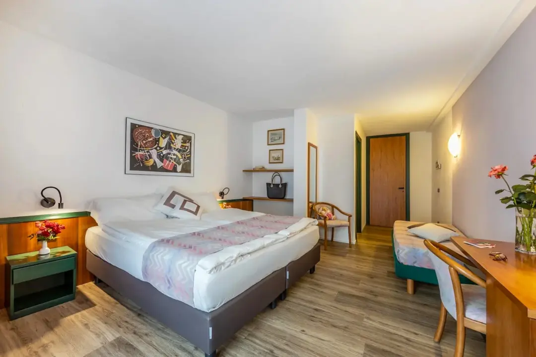 Unmade double bedroom interior with bed, dining table and chair, and wall art