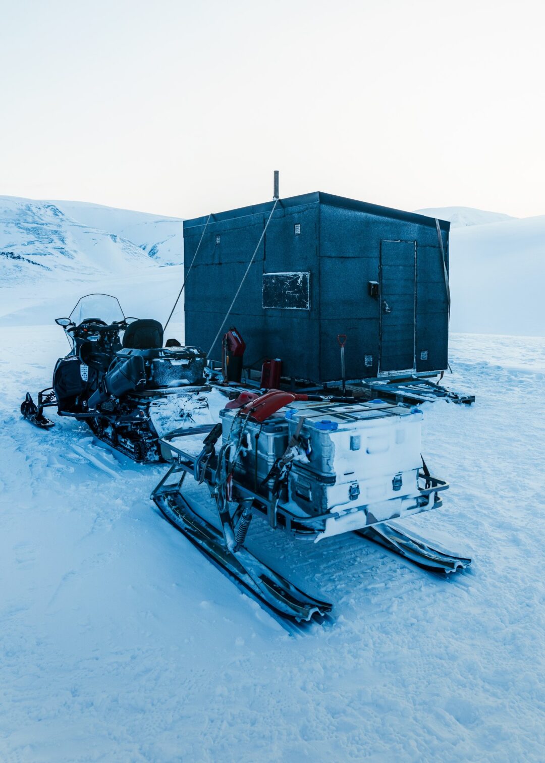 Snowmobile with gear and a blue shelter in a snowy arctic landscape