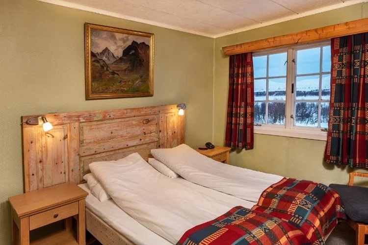 Wooden-framed double bed in a cosy hotel room with window view and patterned blankets