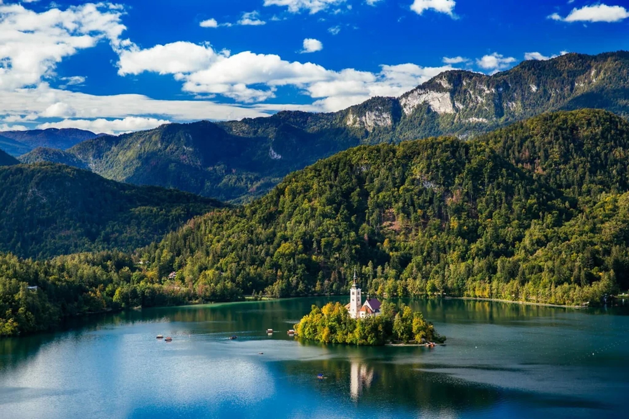 Scenic lake in Slovenia with a small island church and forested mountain ridges under blue skies