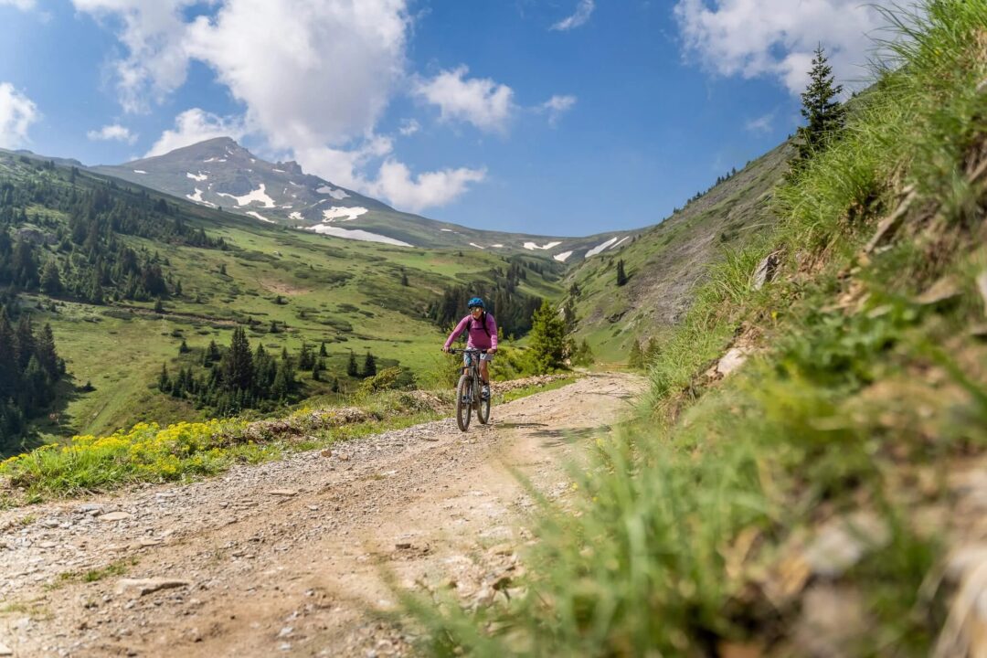 Woman mountain biking along a rocky Alpine trail with snow-capped peaks in the distance