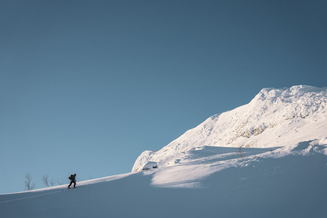 Ski tourer climbing a snowy mountain slope under a clear blue sky