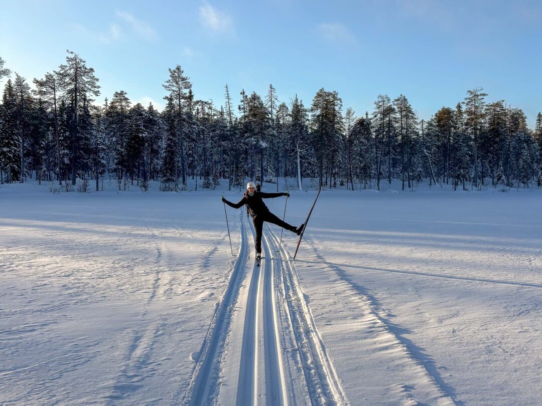 Woman cross-country skiing on a snowy track through pine forest in winter sunshine