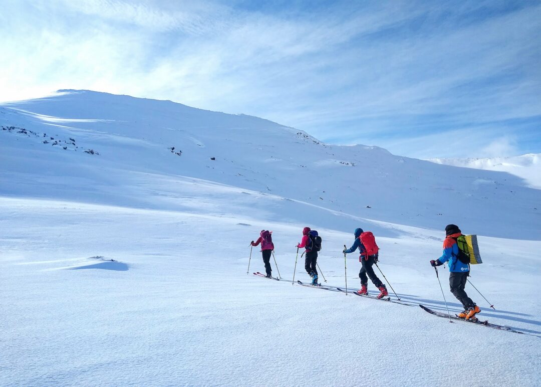 Women ski touring across snowy mountains in Norway, walking uphill on skis with backpacks